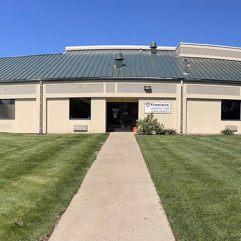 Front view of a single-story beige building with green roof and a walkway to the entrance.