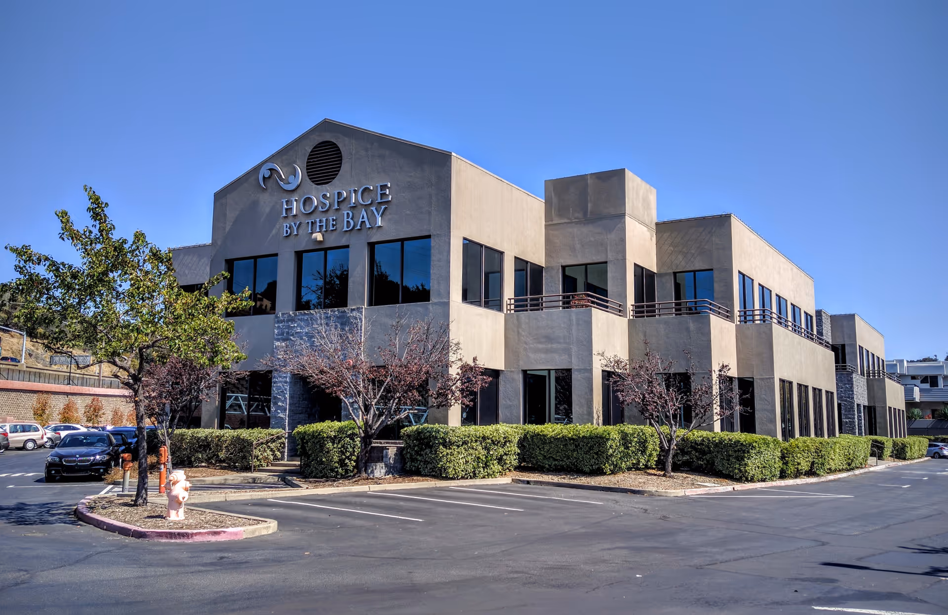 Exterior view of Hospice By The Bay building with a parking lot.