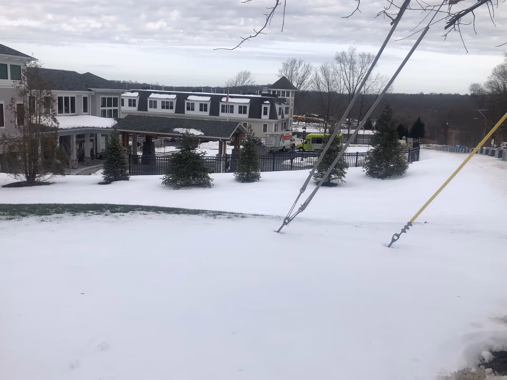Snow covers the front exterior of Ridgefield Station Senior Living, with trees and a gated entrance.