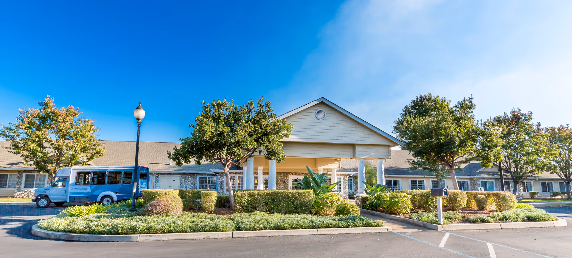 Exterior view of Brookdale Kettleman Lane with entrance, bus, and landscaped front.