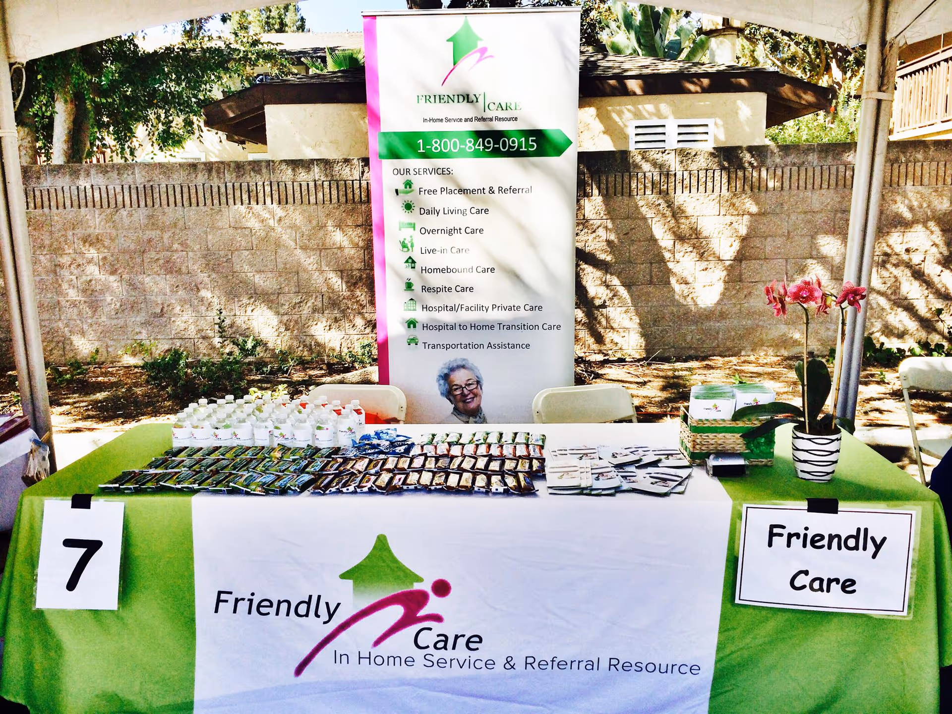 Outdoor info booth with a green tablecloth, banner, and promotional materials for Friendly Care.