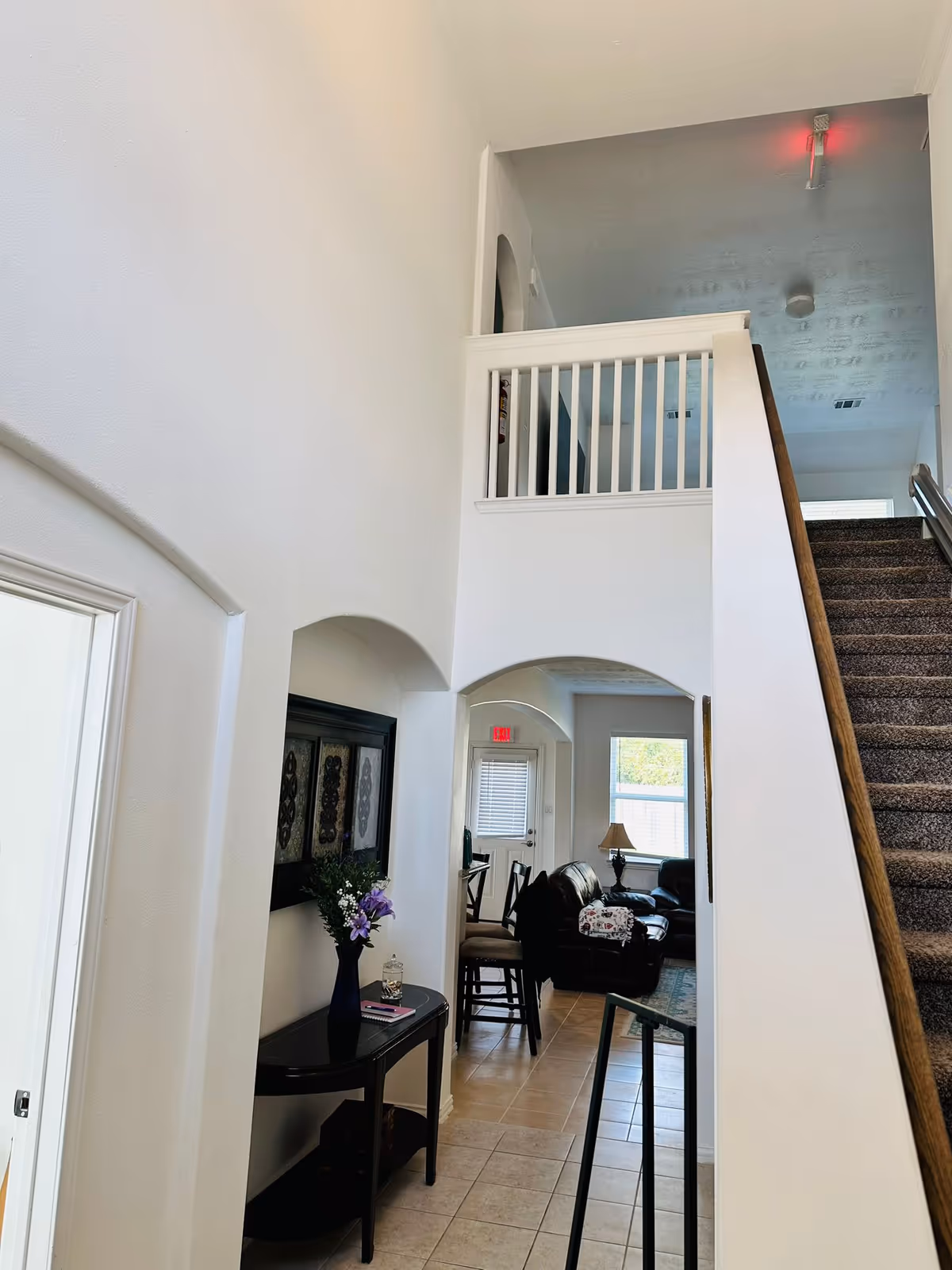 Two-story, white-walled foyer with a stairway, archways, and a seating area in the background.
