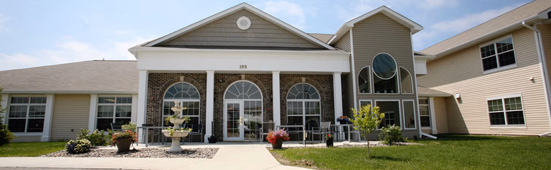 Exterior of Traditions of Owatonna senior living facility with brick facade and arched glass doors.