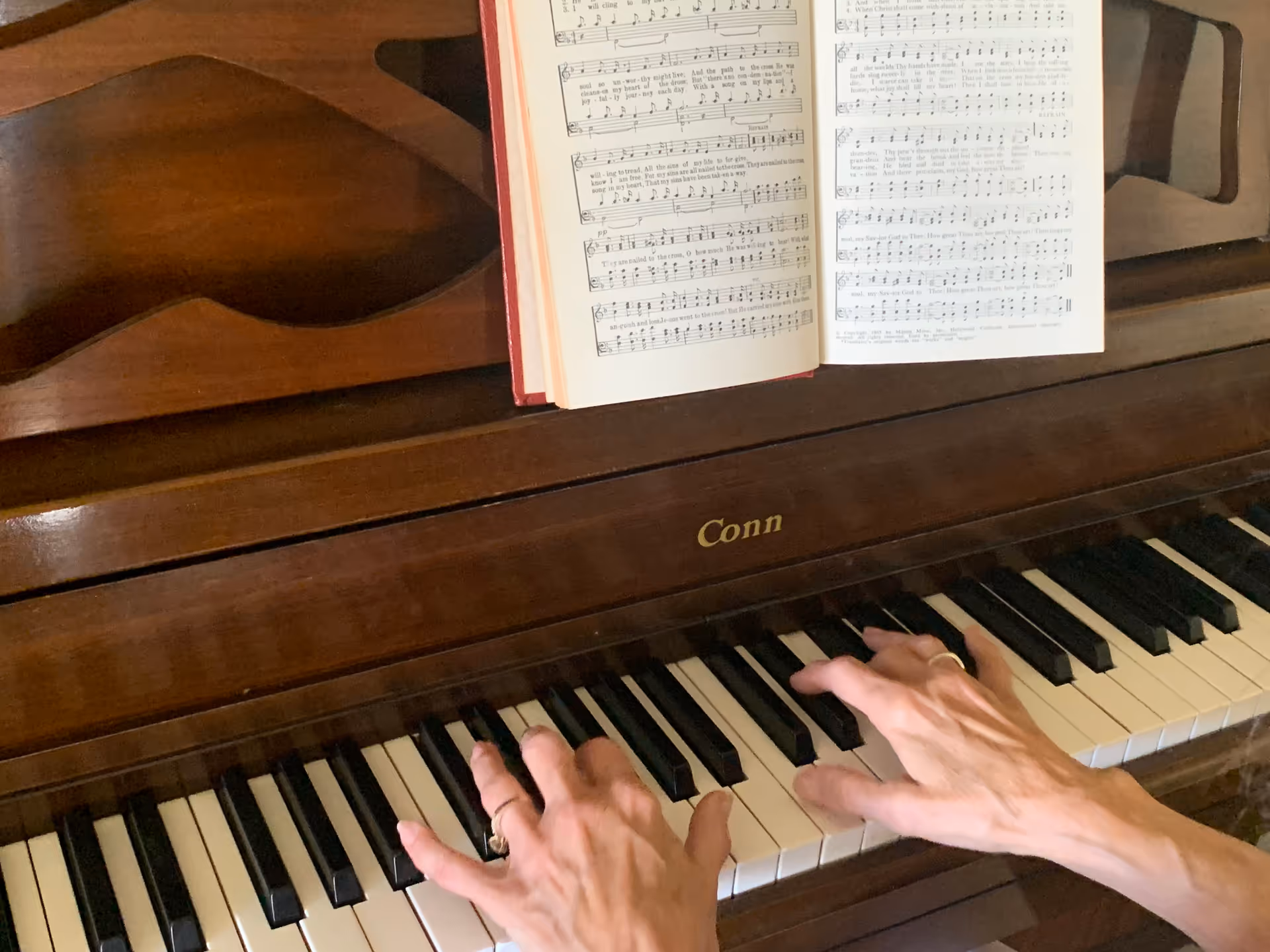 A pair of hands plays a wooden piano with sheet music resting on top.