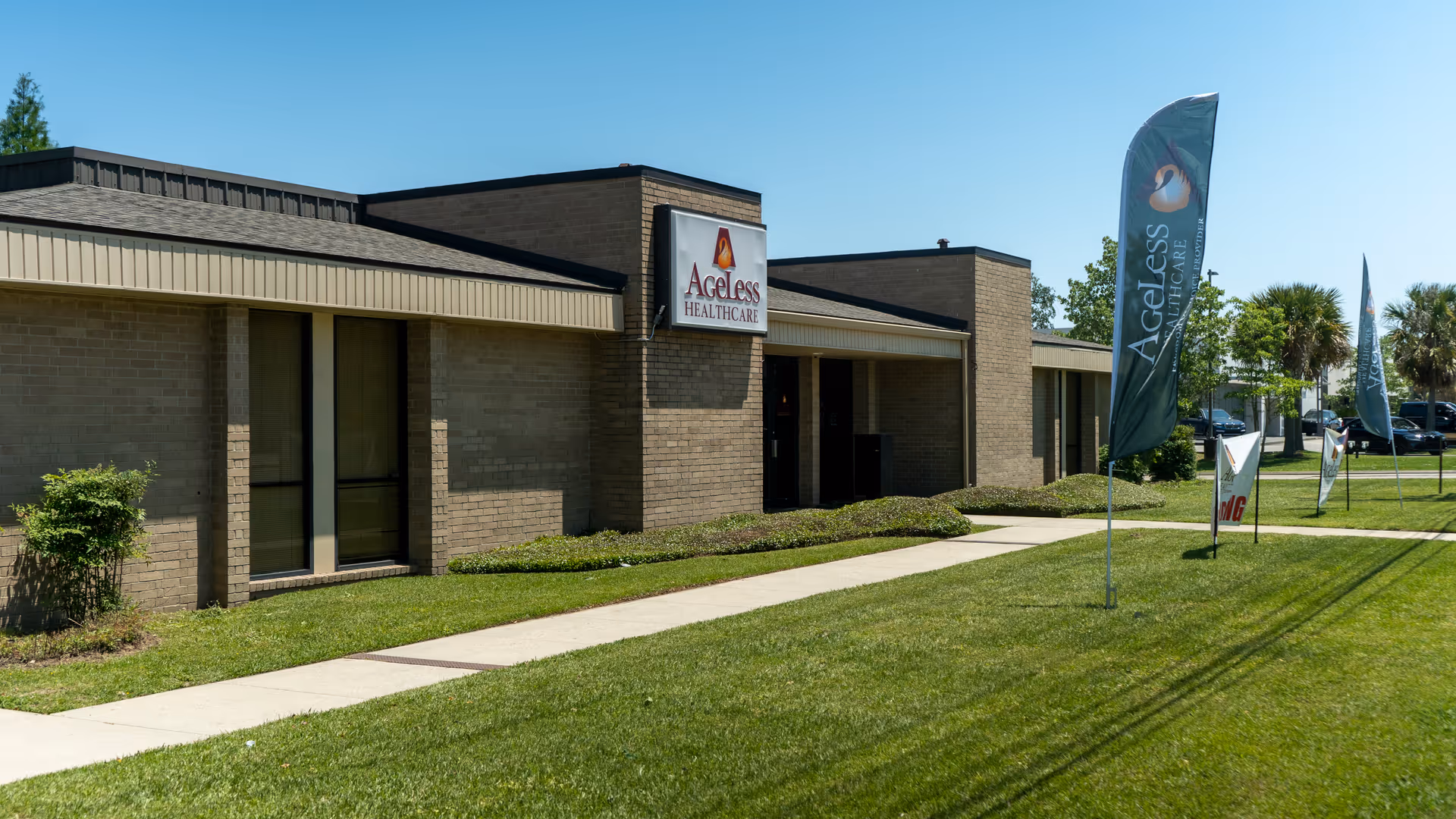 Brick senior care facility exterior with Ageless Healthcare sign and tall blue banners.