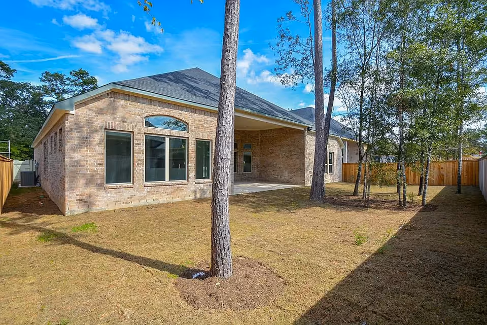 Exterior view of a single-story brick building with large windows, trees, and a fenced yard.