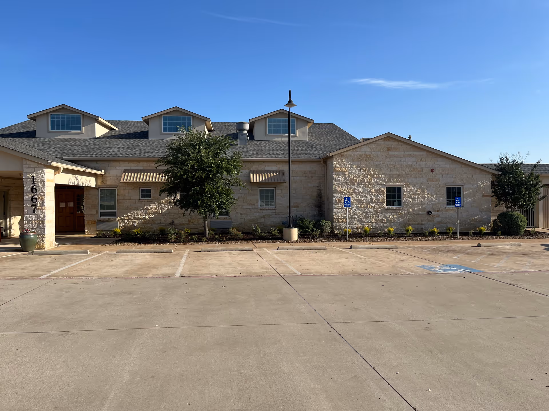Exterior of Bader House Memory Care building with parking lot and landscaping under clear blue sky.