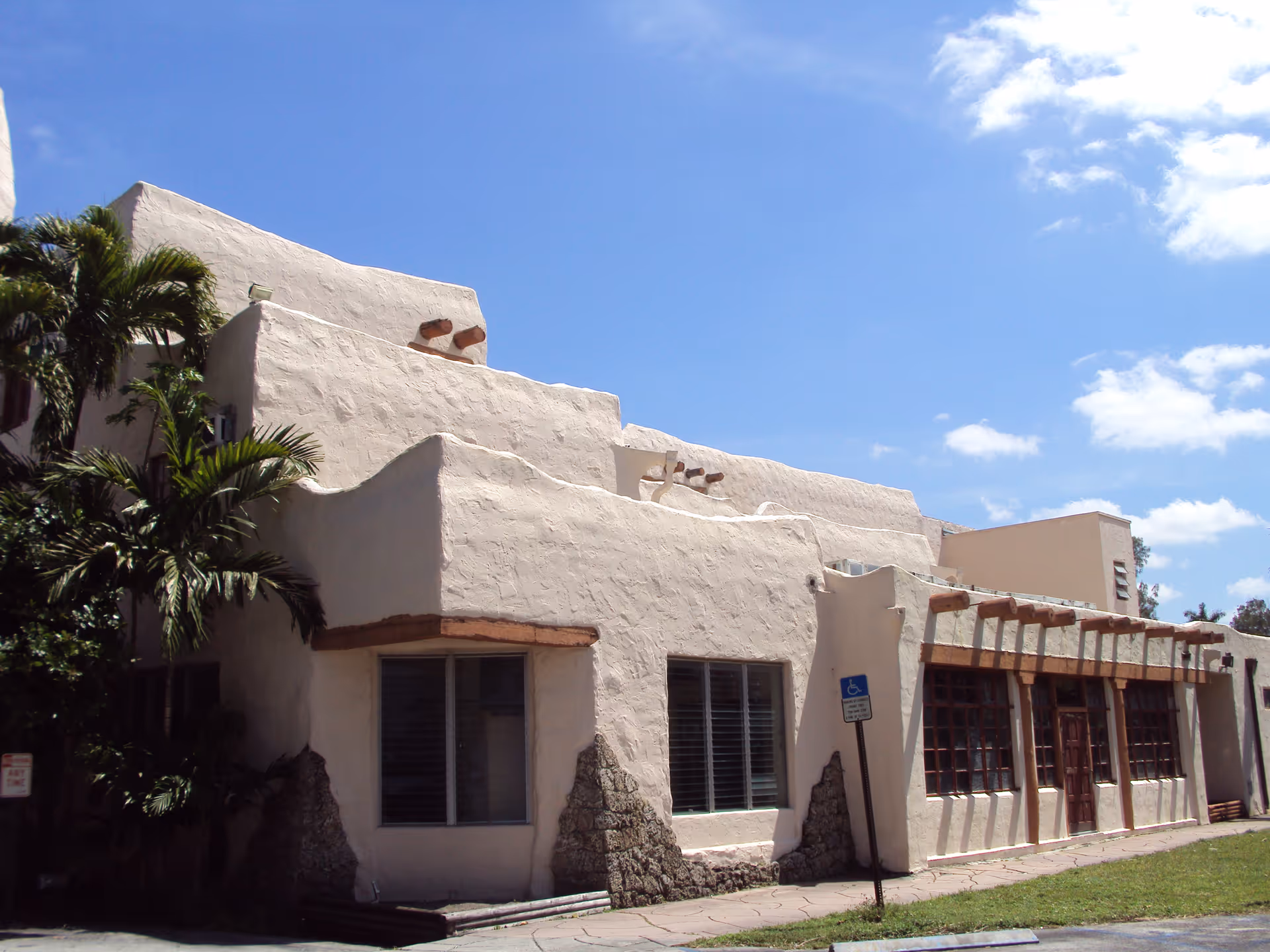 Exterior view of a beige adobe-style facility with palm trees and multiple windows.