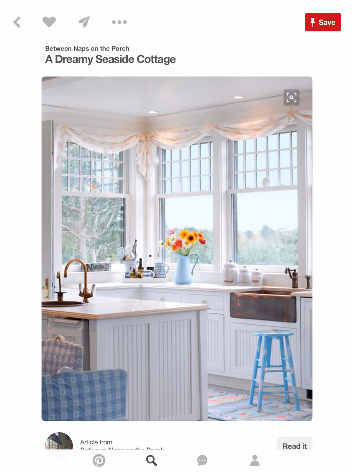 Bright white kitchen with island, faucet, and large windows overlooking outdoors.