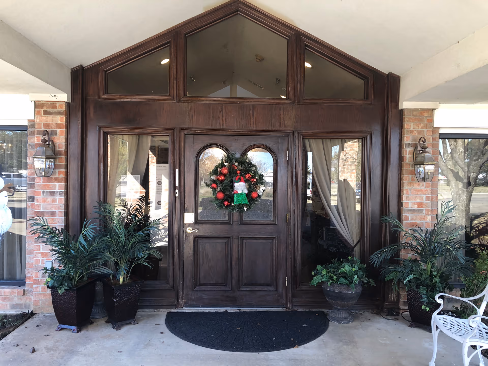 Crestwood Assisted Living entrance: wooden front door with wreath, brick columns, and potted plants.