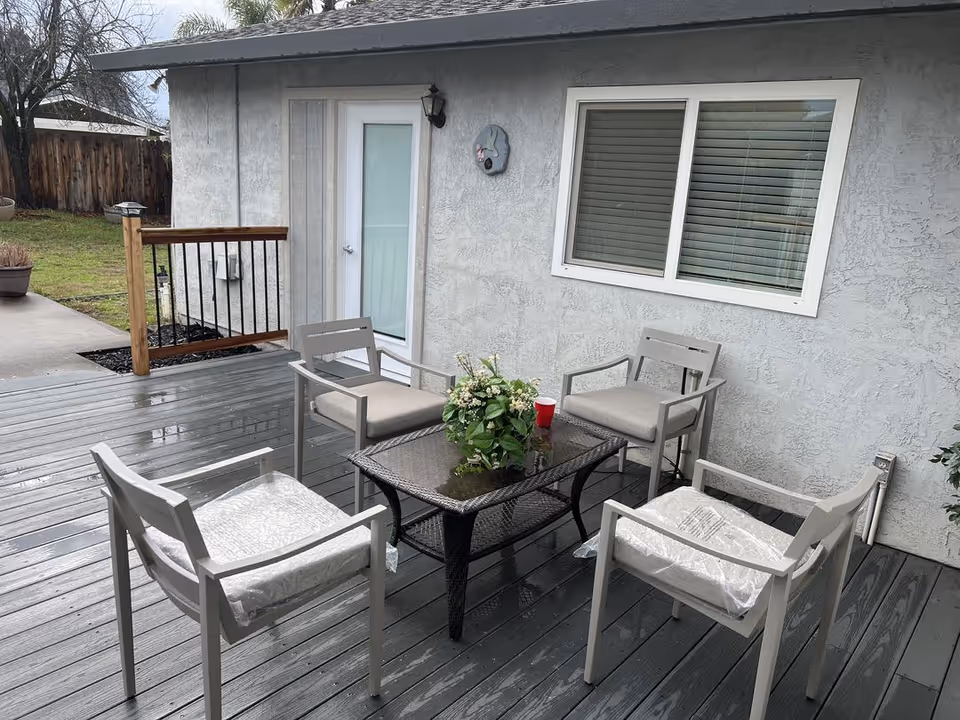 Outdoor patio with four chairs around a glass table beside a grey building.