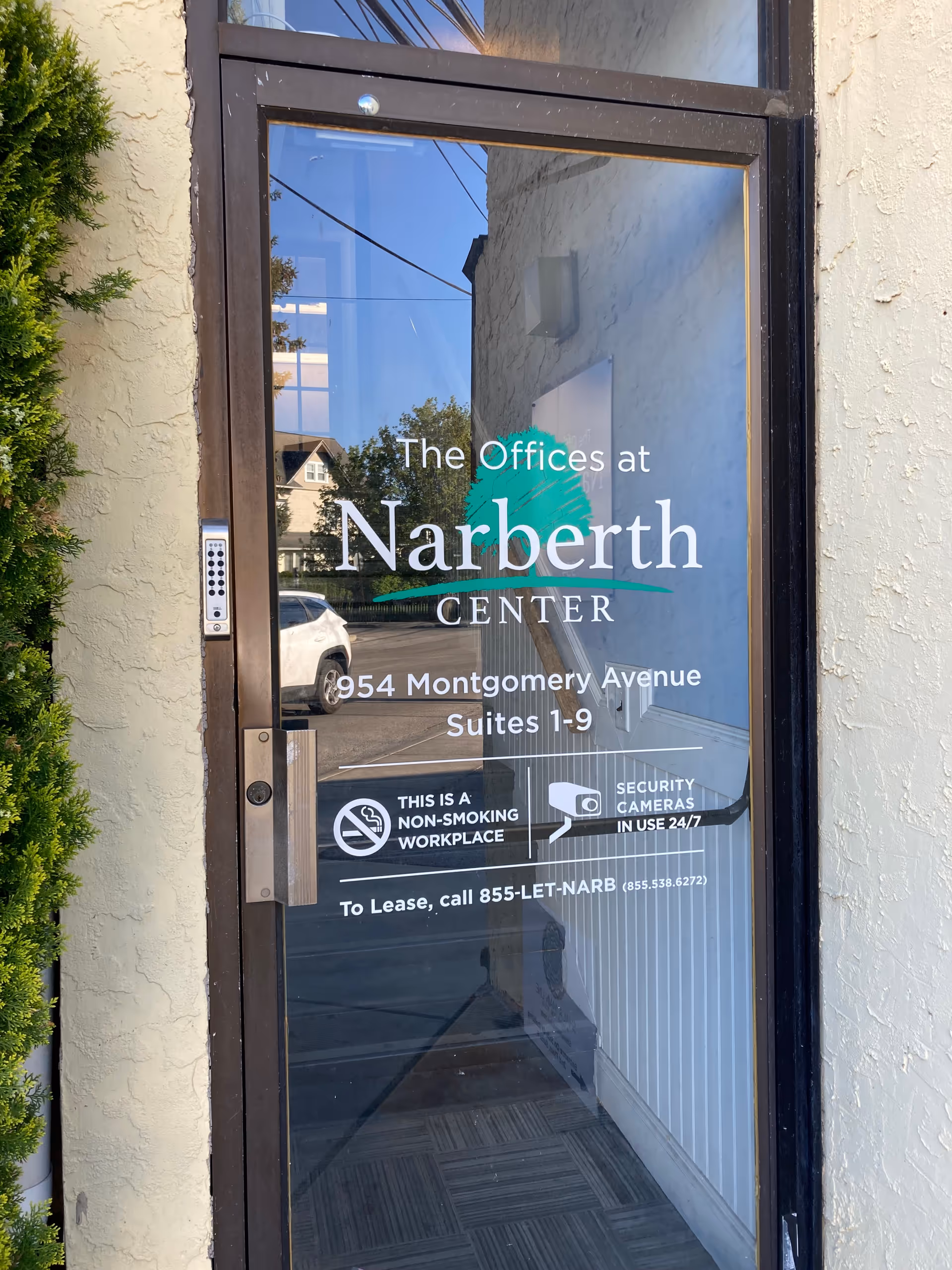 Glass door entry displaying Narberth Center offices signage and street reflection.
