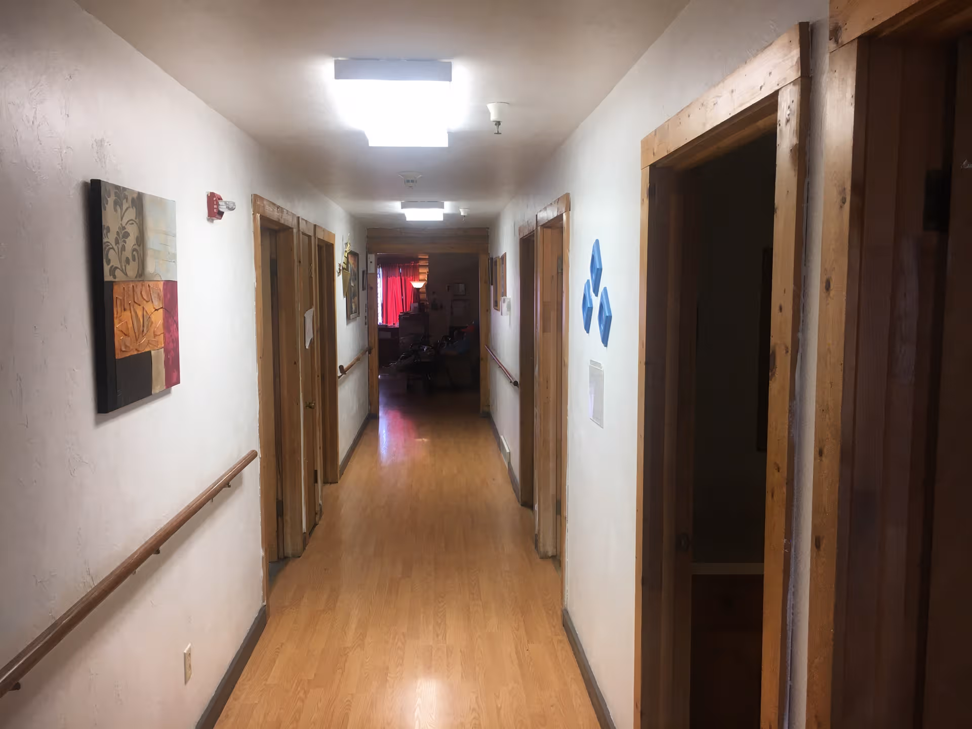 Long hallway inside a senior living facility with wooden doors, handrails, and wall art.