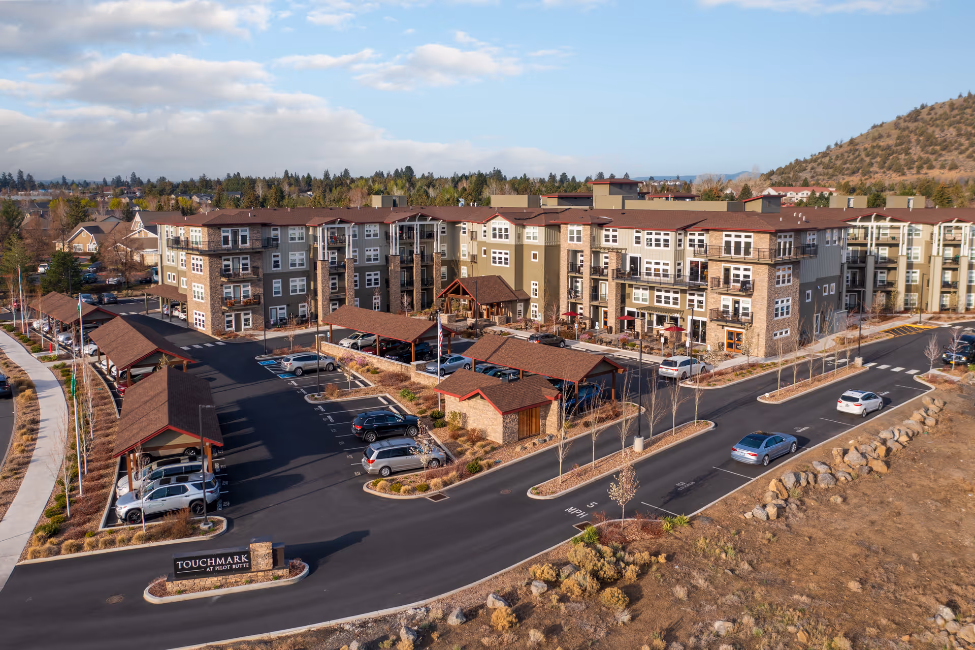 Aerial view of the Touchmark at Pilot Butte senior living building with parking, covered carports, and an entrance sign.