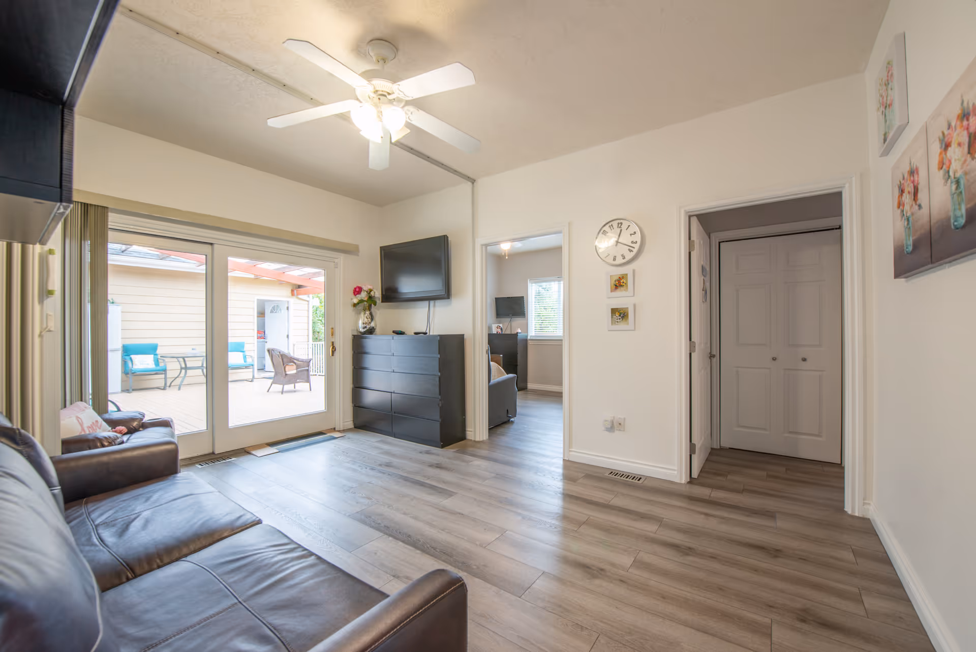 Bright living room featuring leather sofas, sliding glass doors to a patio, and a wall clock.
