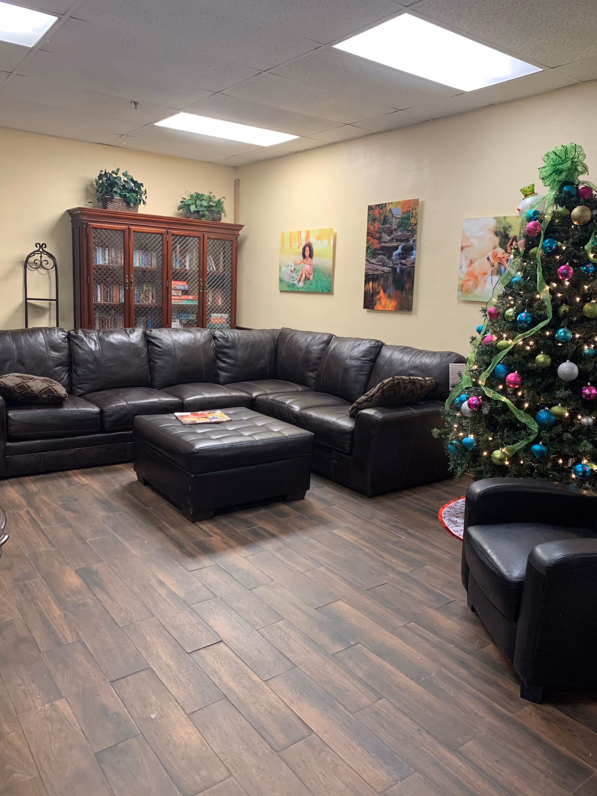Cozy indoor living room with a black leather sectional, ottoman, and a decorated Christmas tree.