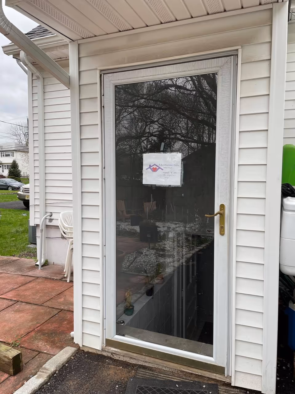 Glass door of a senior living facility with a posted sign, exterior siding and patio seating.