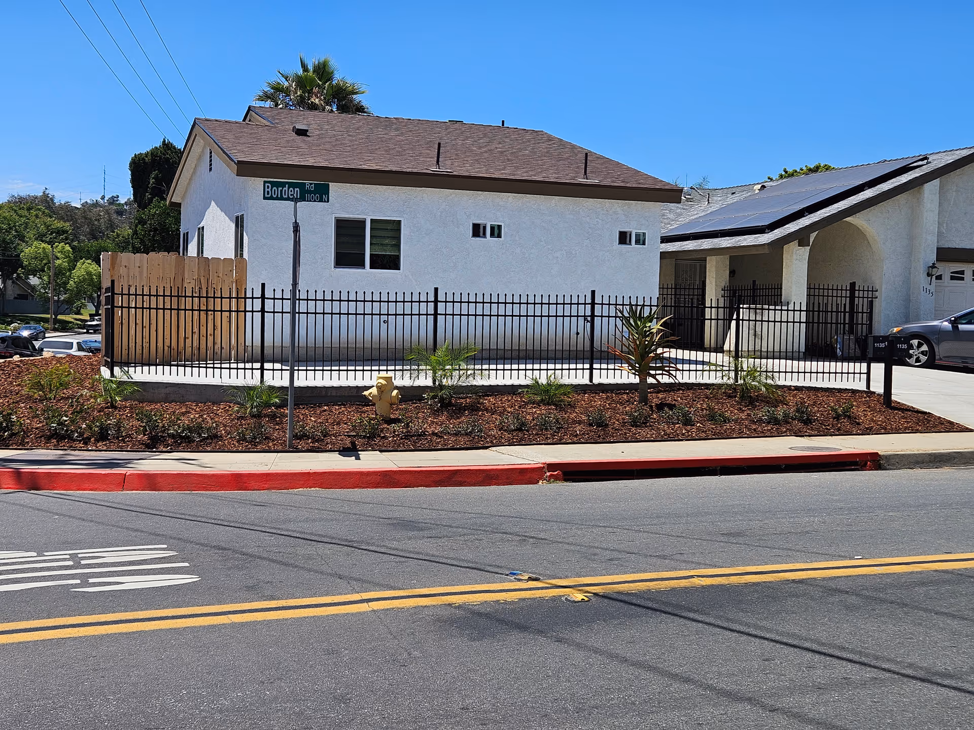 White single-story building with black metal fence and landscaped front yard along a street.