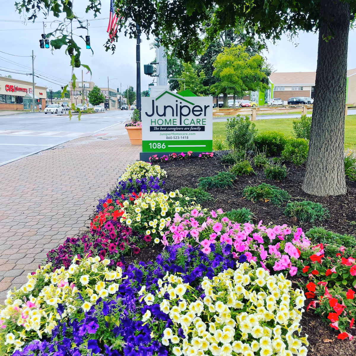 Juniper Home Care sign on a landscaped sidewalk with vibrant flowers and a tree-lined street