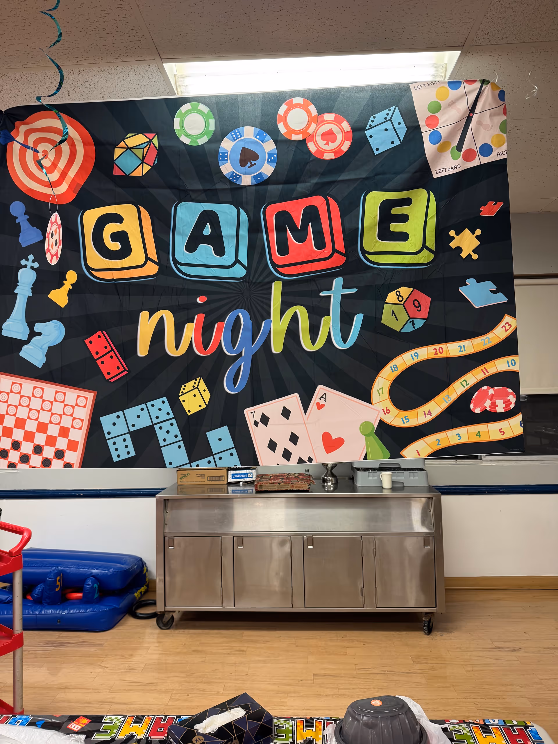 Colorful 'Game Night' banner on wall with metal cabinet and floor in a rec room.