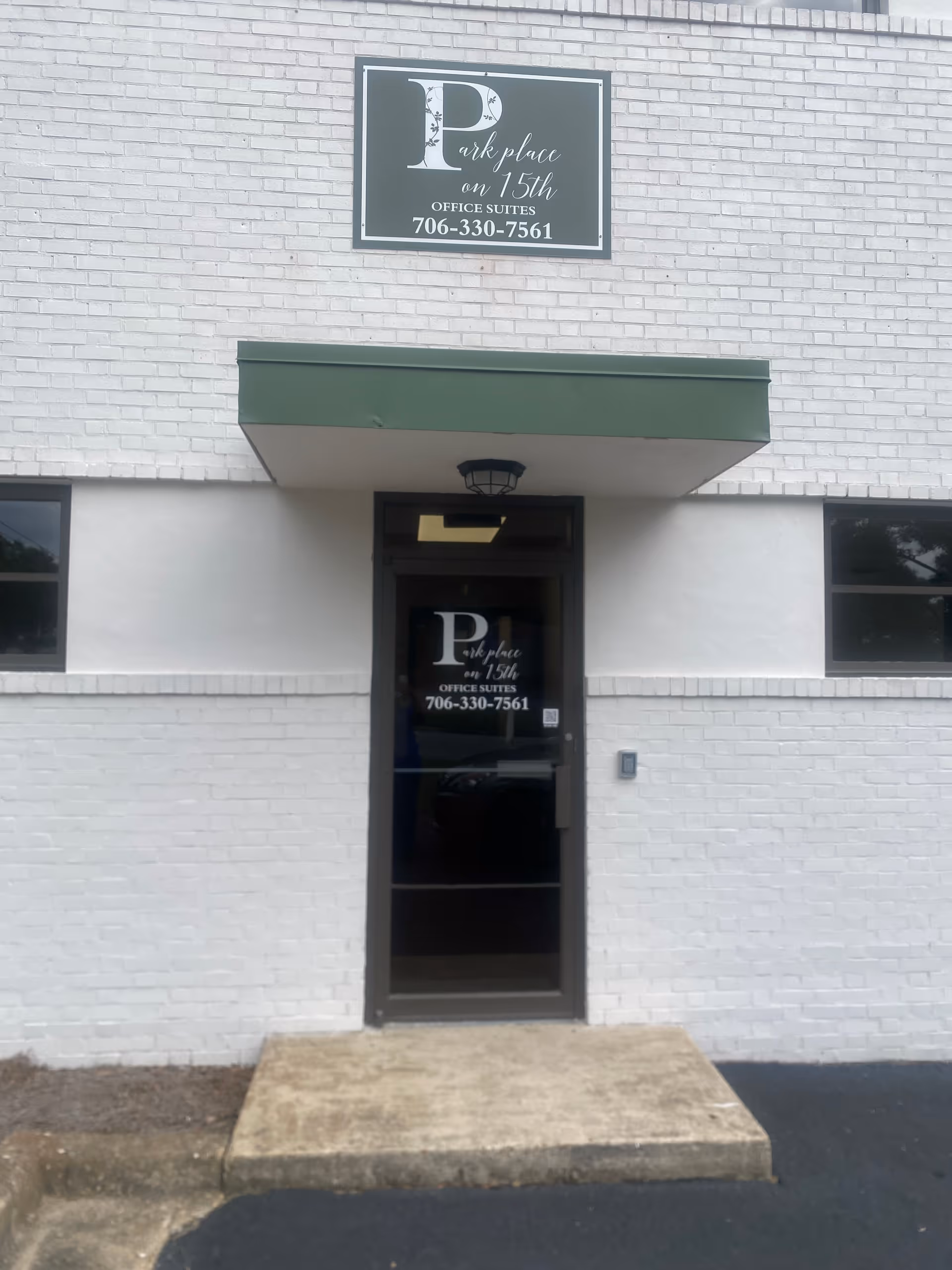 White brick building exterior featuring a glass door entrance and a green awning.