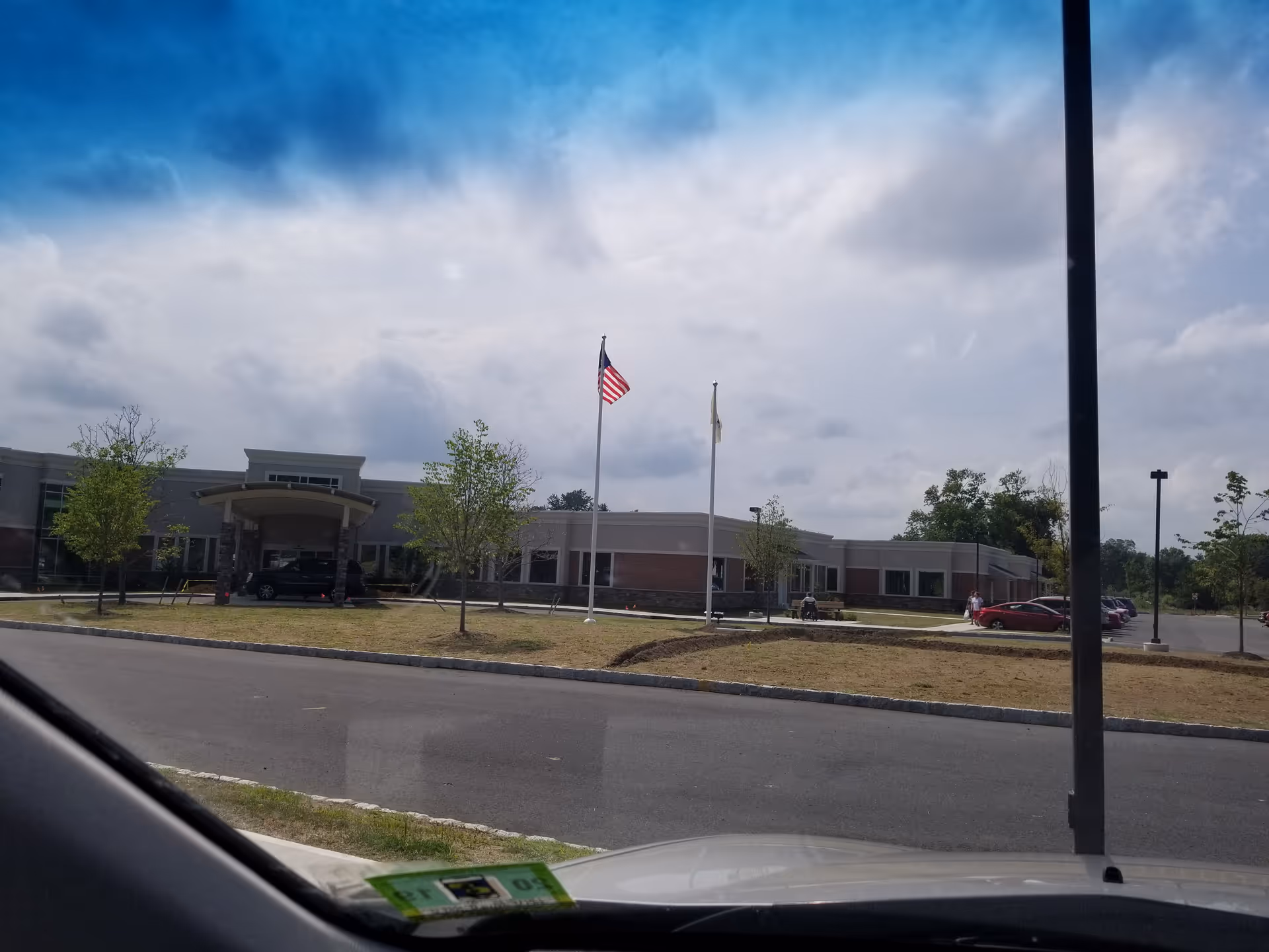 Exterior view of Atlas Post Acute at Woodbury Country Club, with flagpoles, entrance, and parking.