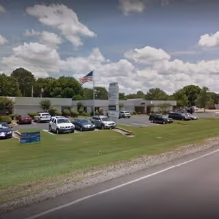 Front view of a single-story building with a parking lot, flag, and sign.