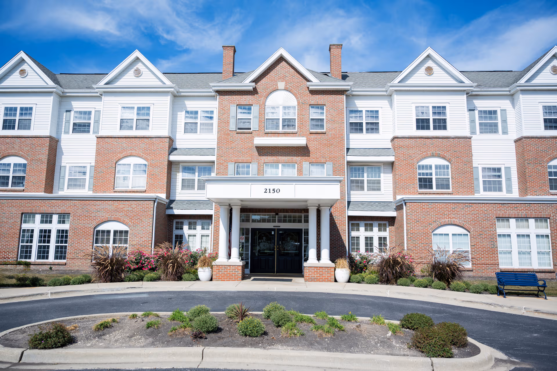 Brick senior living building with white accents and a covered entrance, landscaped front.