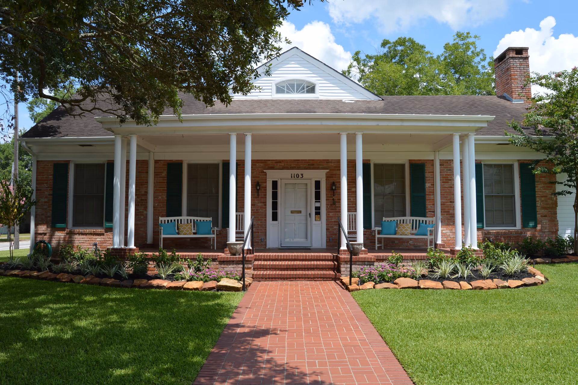 Brick building with a wide front porch, white columns, and seating.
