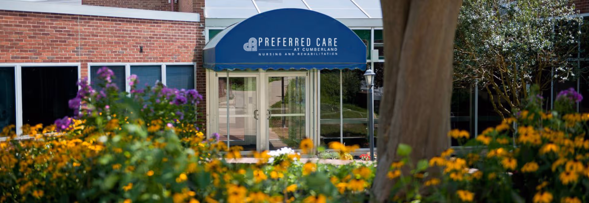 Exterior view of Cumberland Manor entrance with a blue awning and blooming flowers.