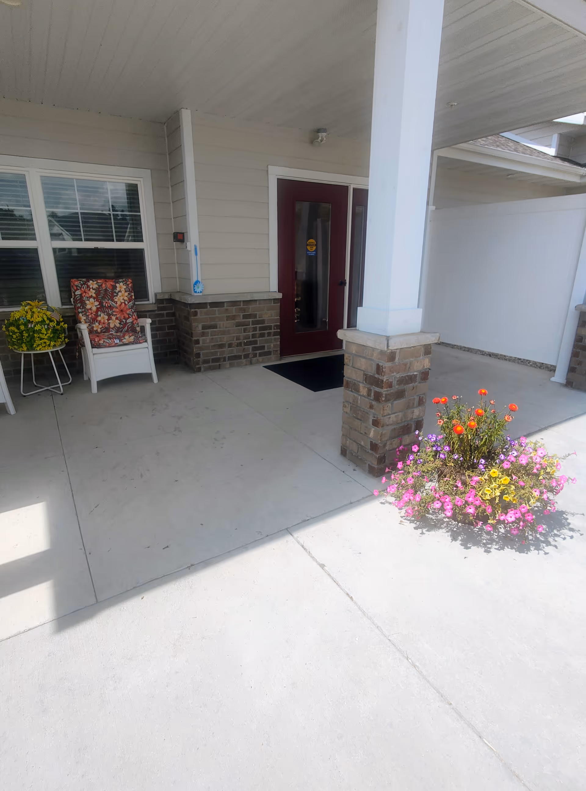 Front entrance of a senior living facility with seating and colorful flowers.