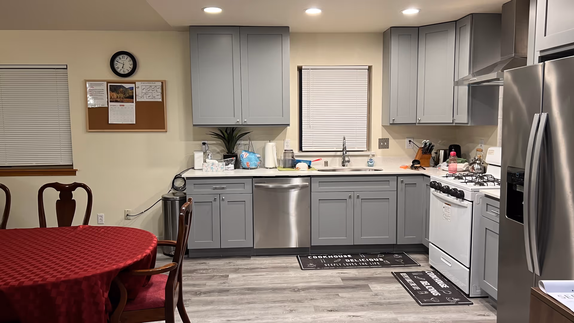 Gray kitchen with stainless appliances, dining table, and window under bright overhead lighting.