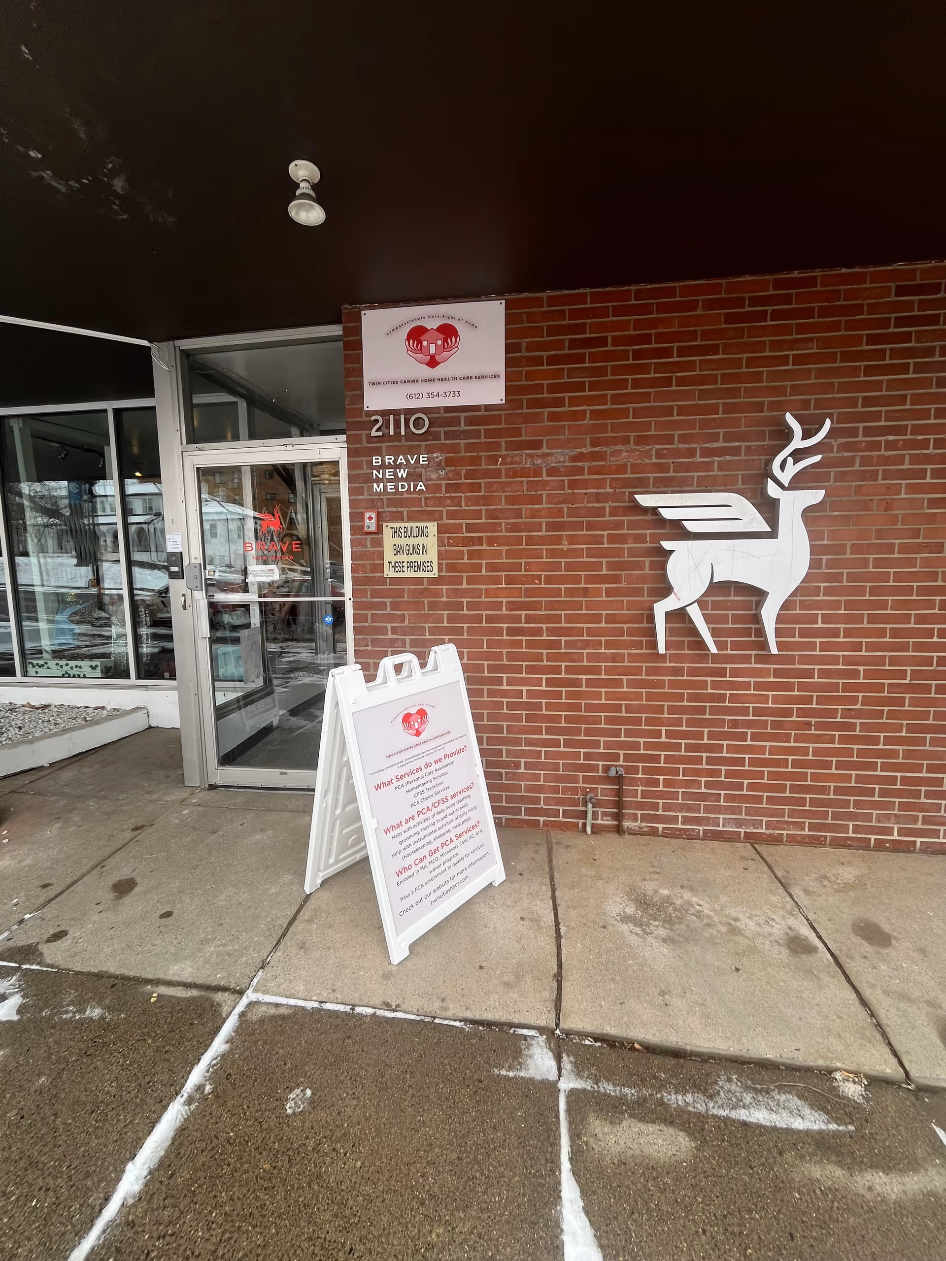 Exterior brick building entrance with glass door, white deer mural, and A-frame sign.