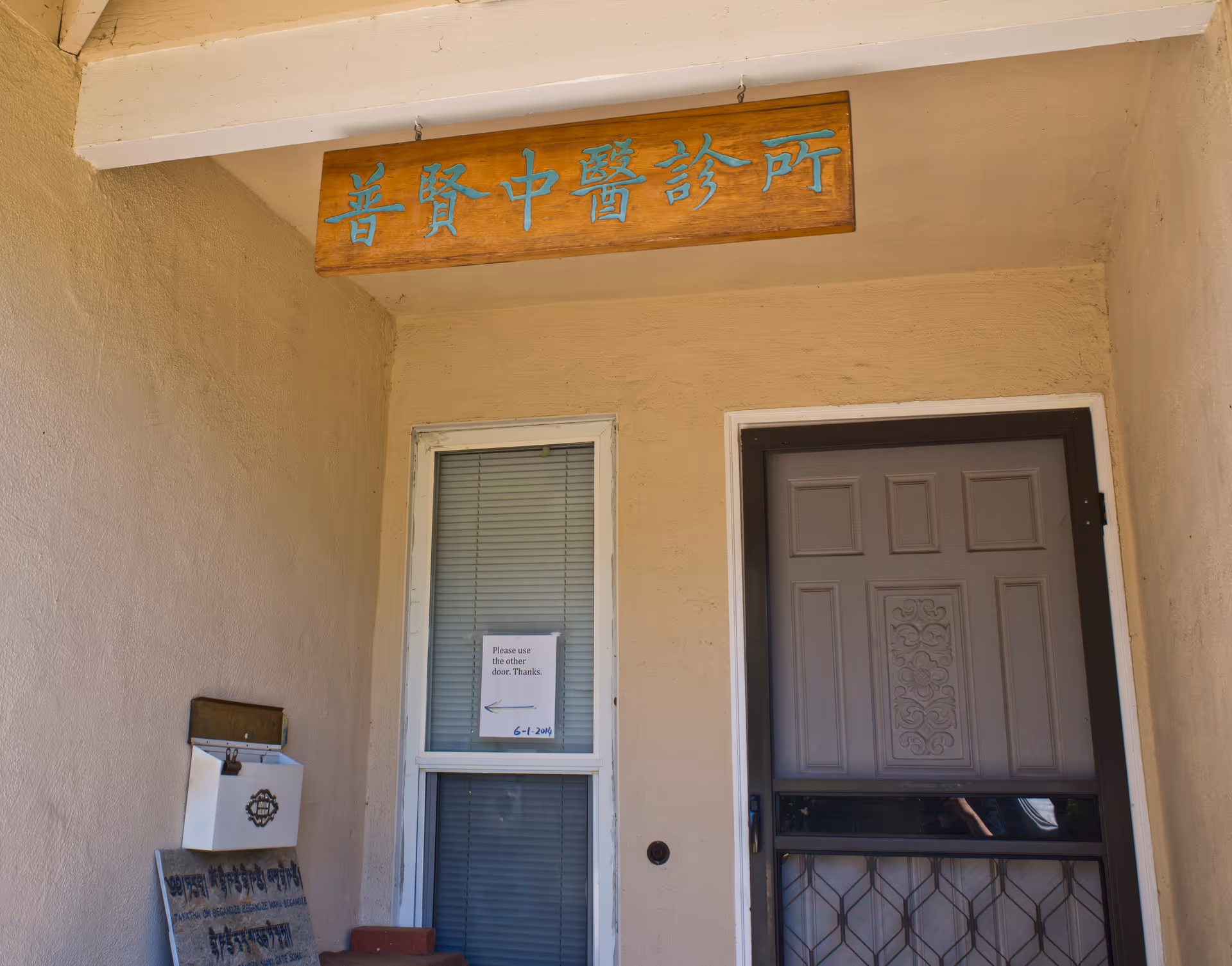 Beige building entrance with a wooden sign and a gray door.