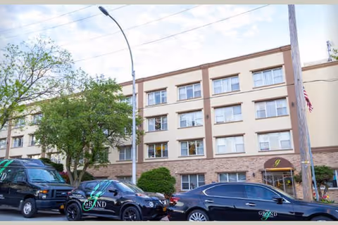 Three-story beige nursing home building with parked cars in front.