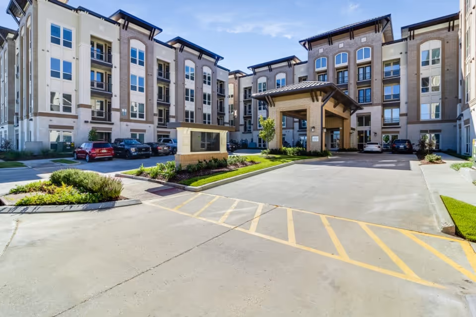 The front entrance and porte-cochère of a multi-story senior living building with landscaped driveway and parked cars.