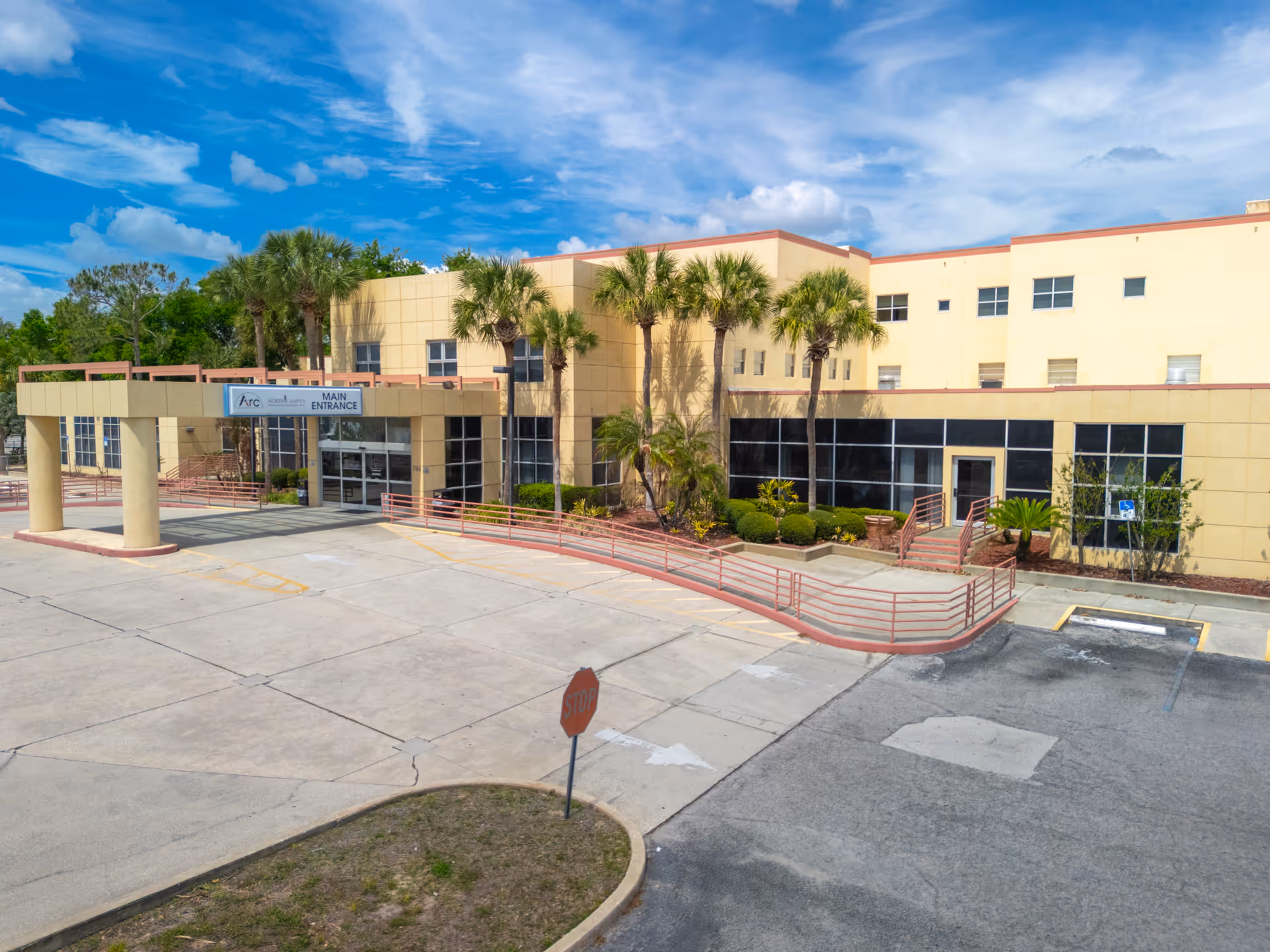 Exterior view of a beige nursing center with palm trees and main entrance.