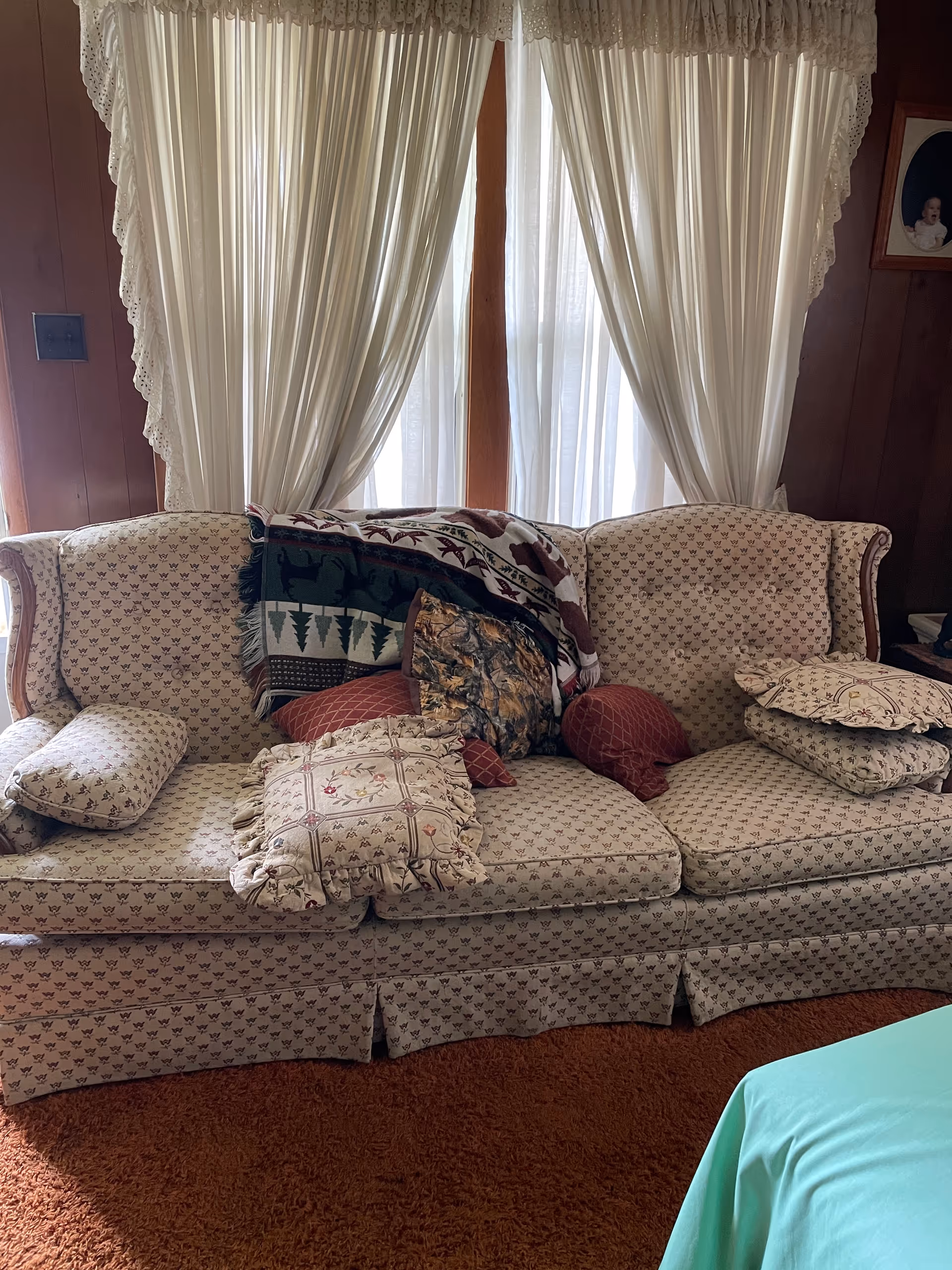Cozy vintage living room with patterned sofa, many cushions, and lace curtains.