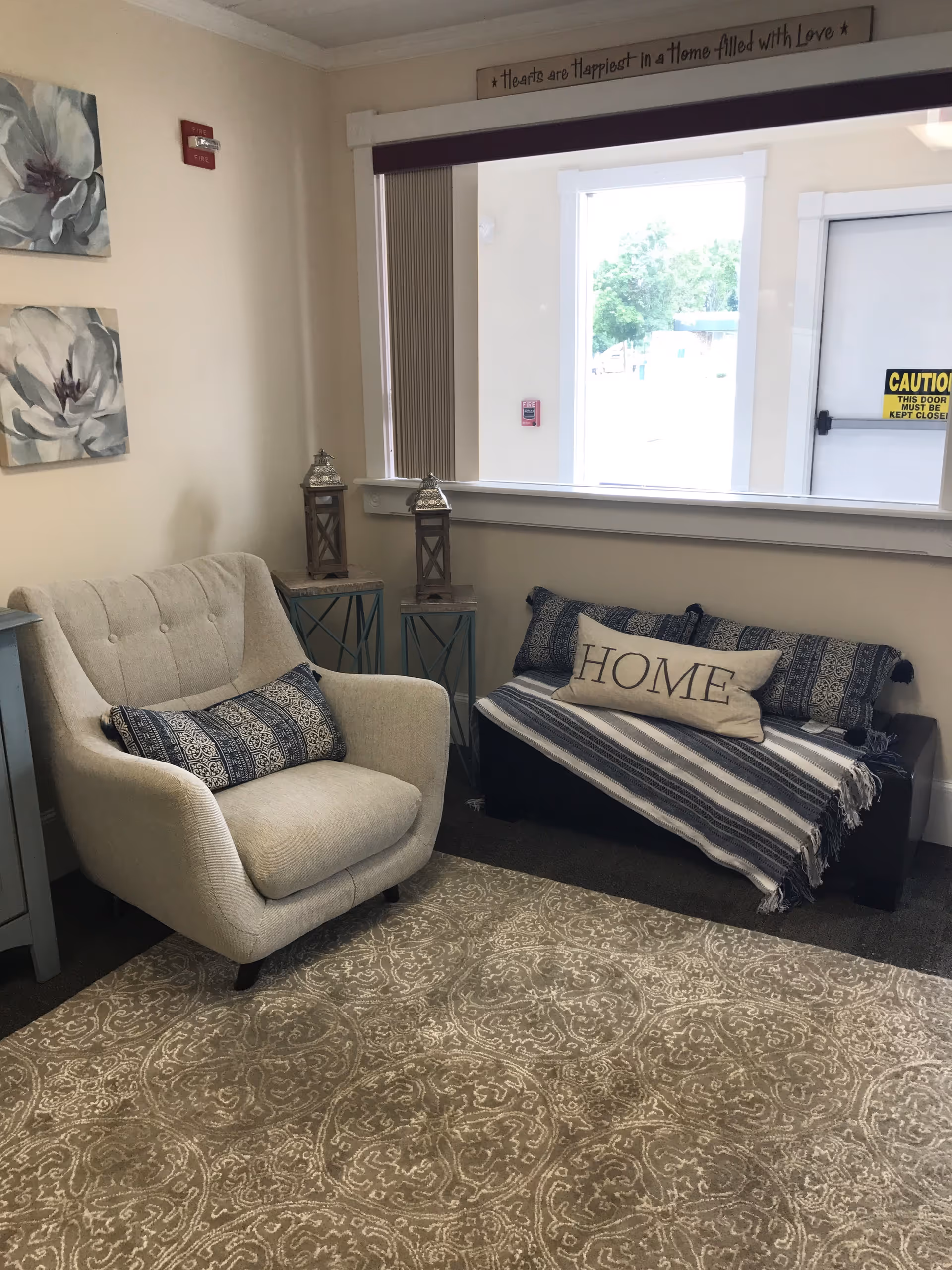 Cozy living room in a senior living facility with armchair, sofa, rug, and window.