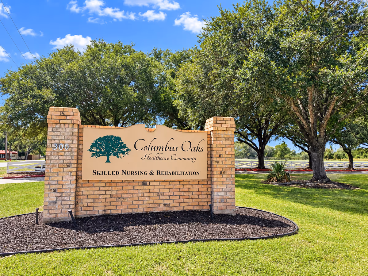 Brick entrance sign for Columbus Oaks Healthcare Community amid trees and lawn.