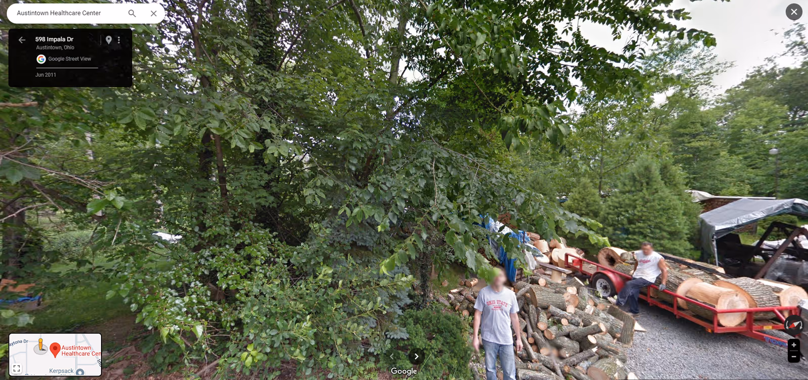Outdoor lumber yard with stacked logs, trailers, and two people near wood piles.