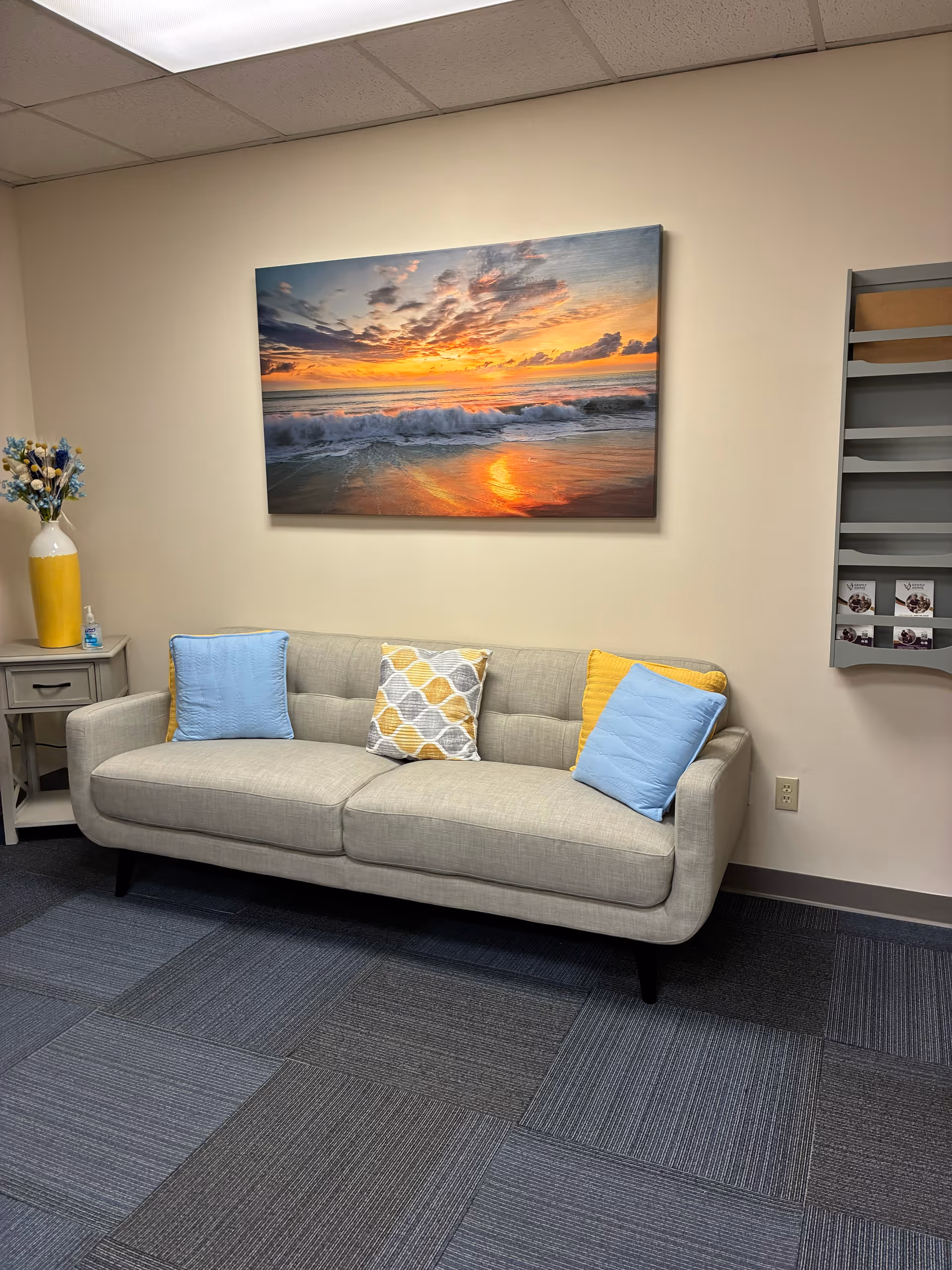 Gray sofa with blue and yellow pillows in a sitting area under sunset art.