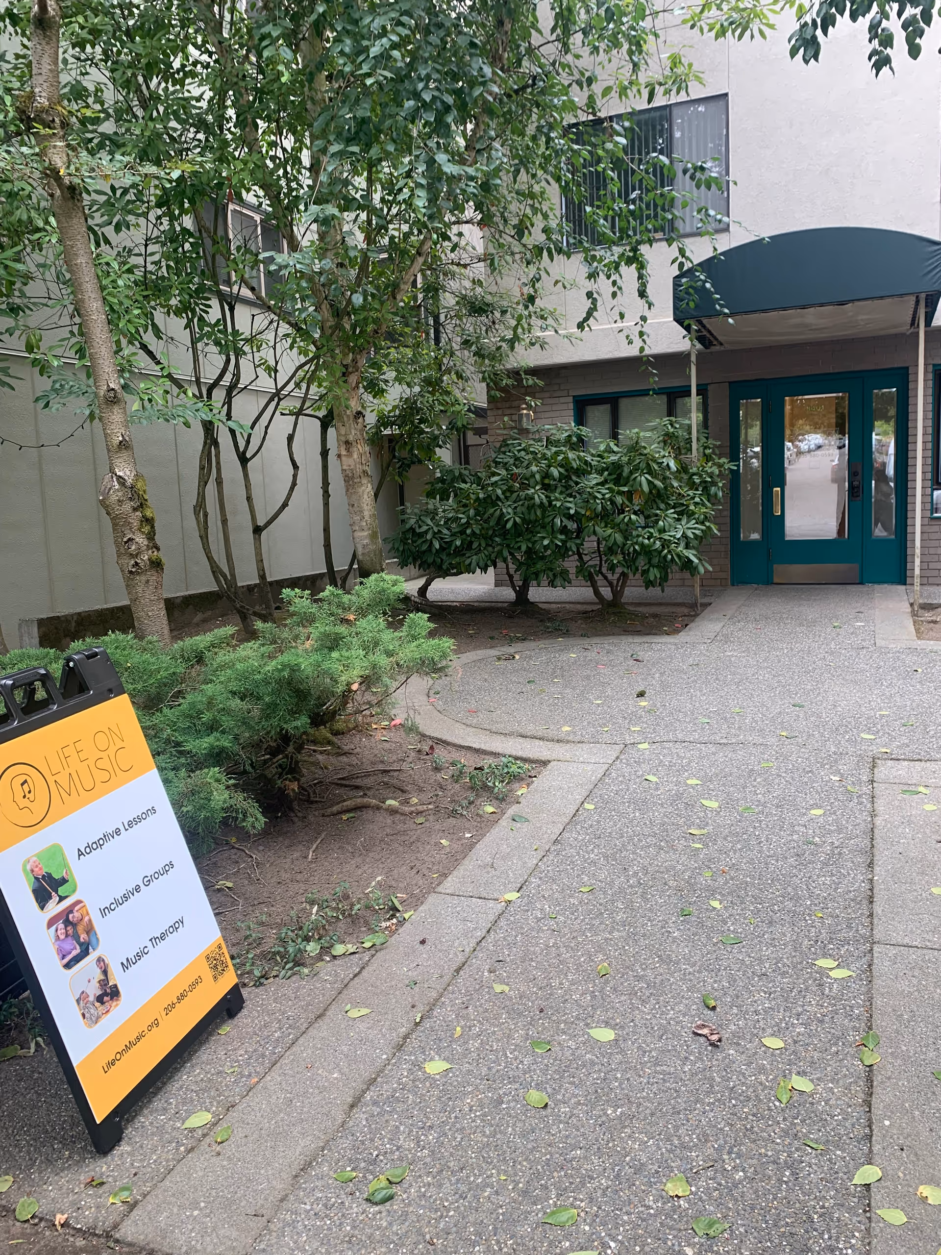 Front entrance of Life On Music facility with teal doors and signboard along walkway.