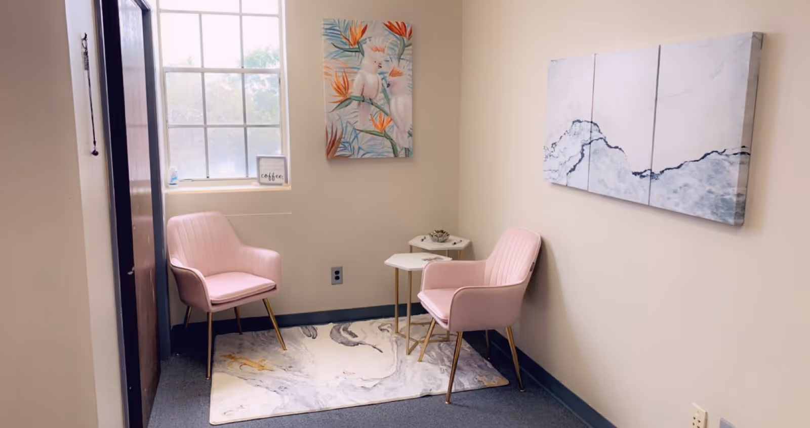 A small interior seating area with two pink armchairs, a rug, and wall art.