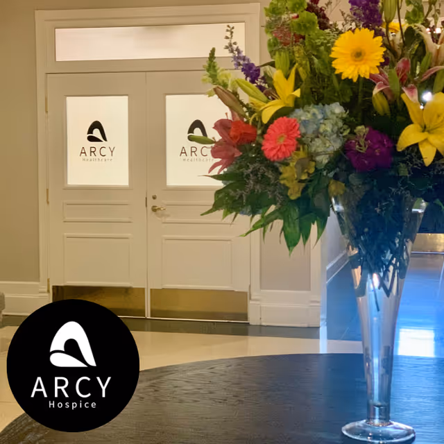 Interior lobby area with double doors displaying ARCY Healthcare logos and a tall flower arrangement.