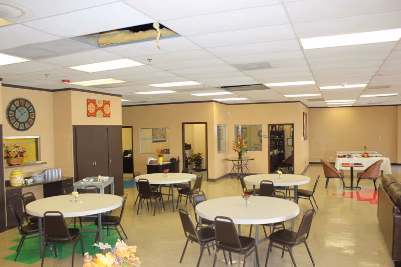 Spacious indoor common dining area with round tables and chairs at Primrose Lane Adult Day Care.