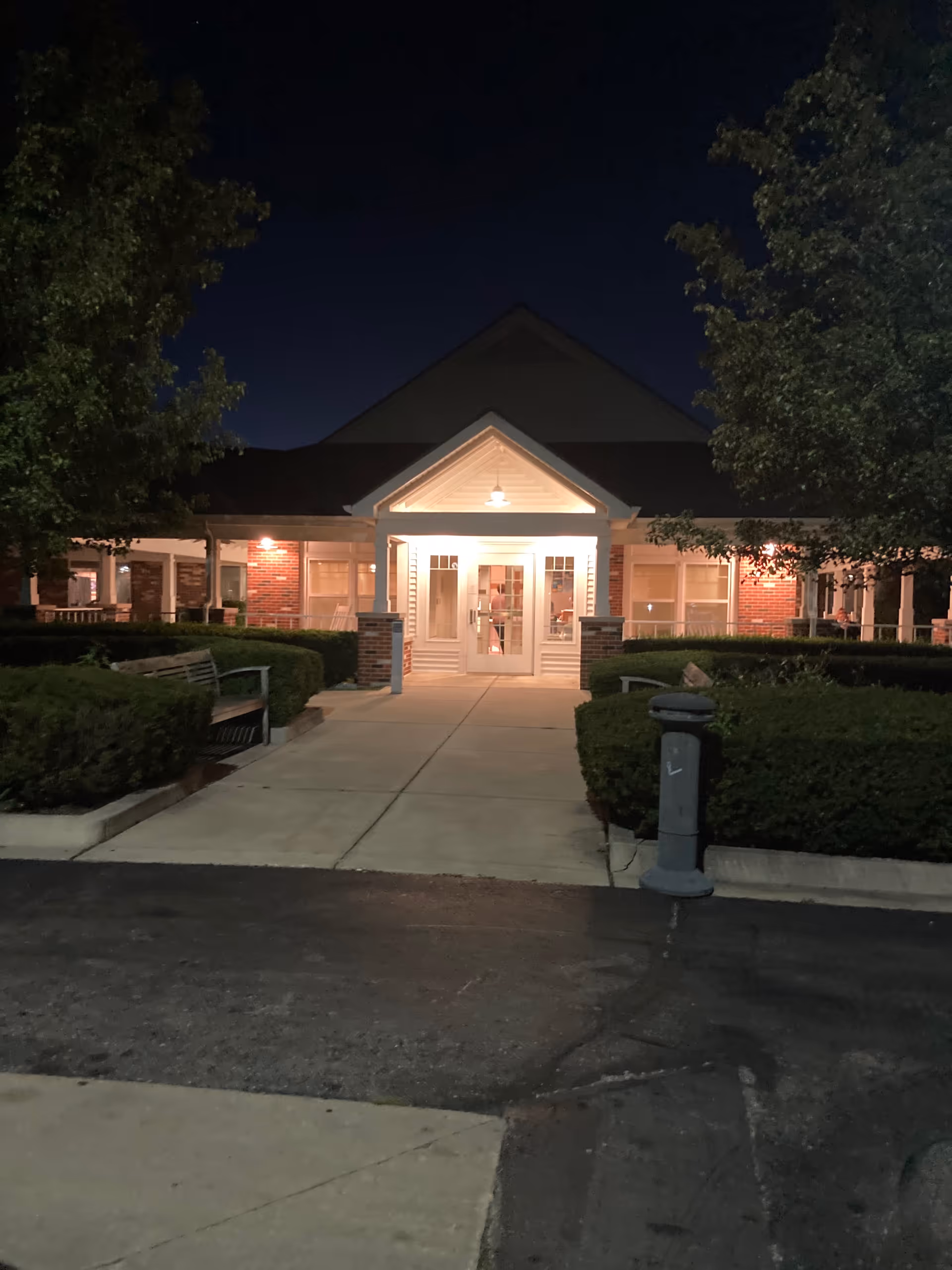 Nighttime exterior of Medilodge of Monroe, lit front entrance surrounded by hedges