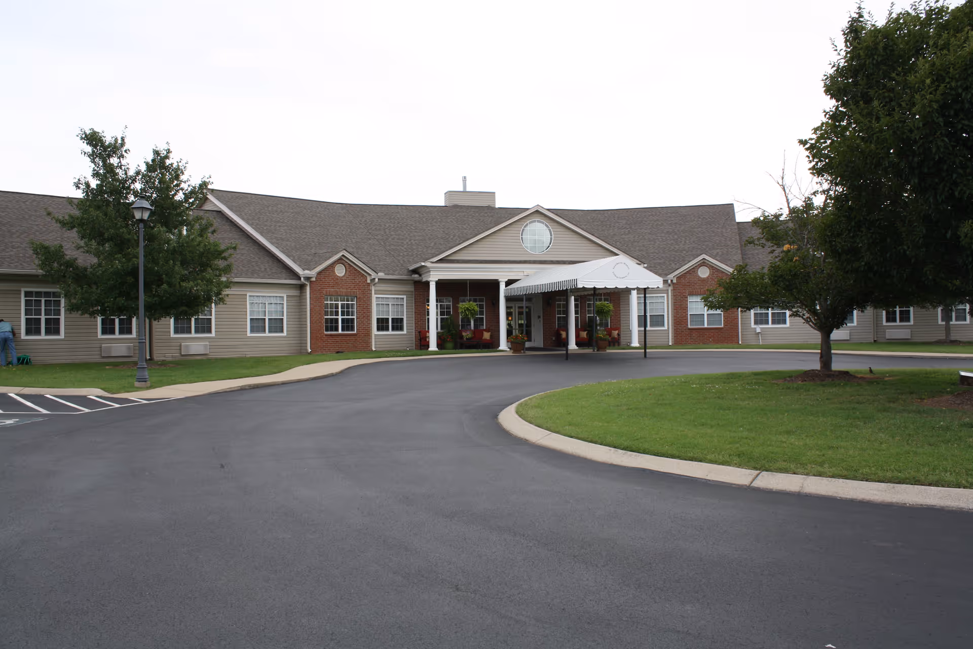 Front view of a single-story senior living facility with a curved driveway and manicured lawn.