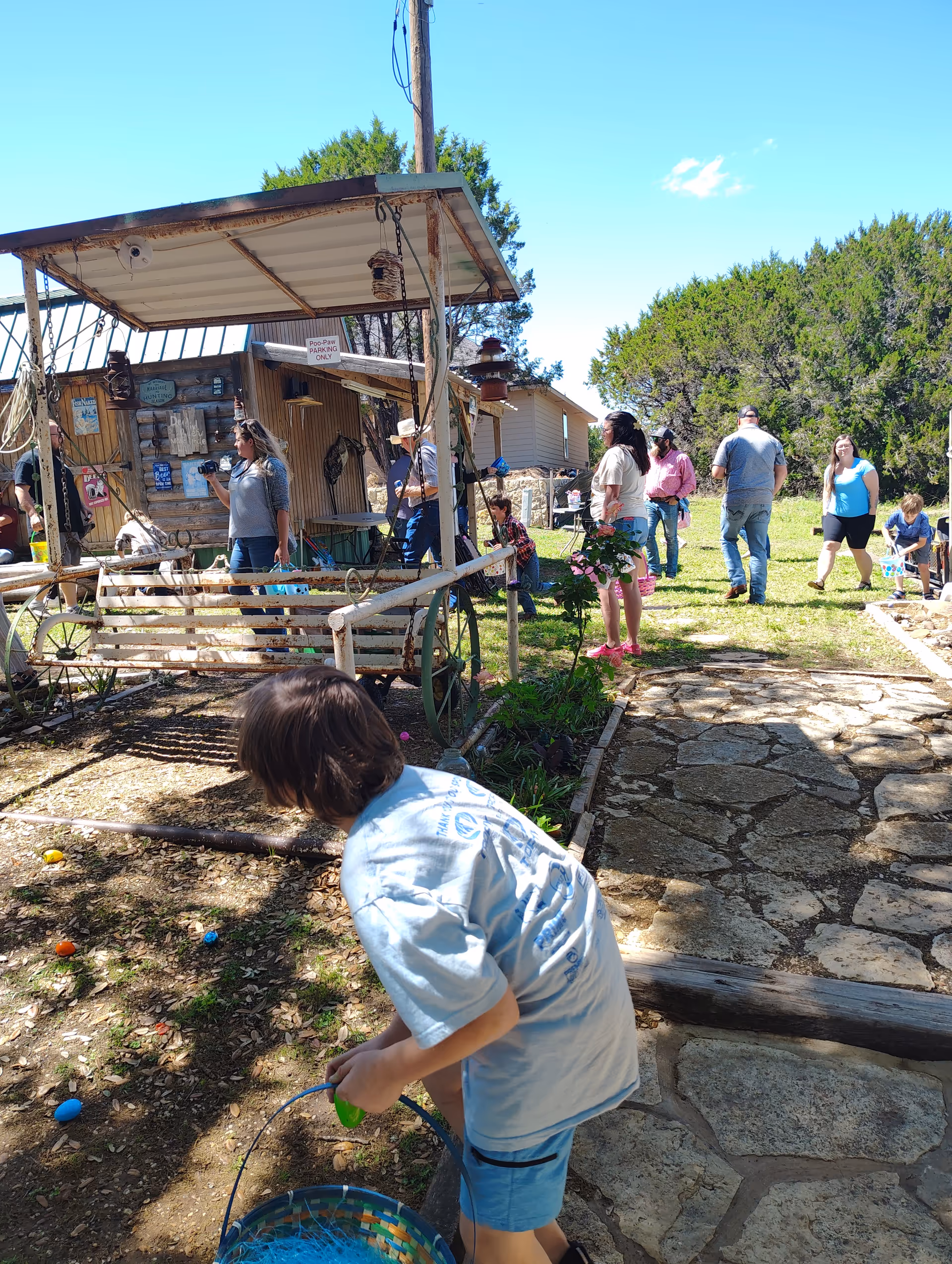 Outdoor community event at a rustic yard with people and a child collecting eggs.