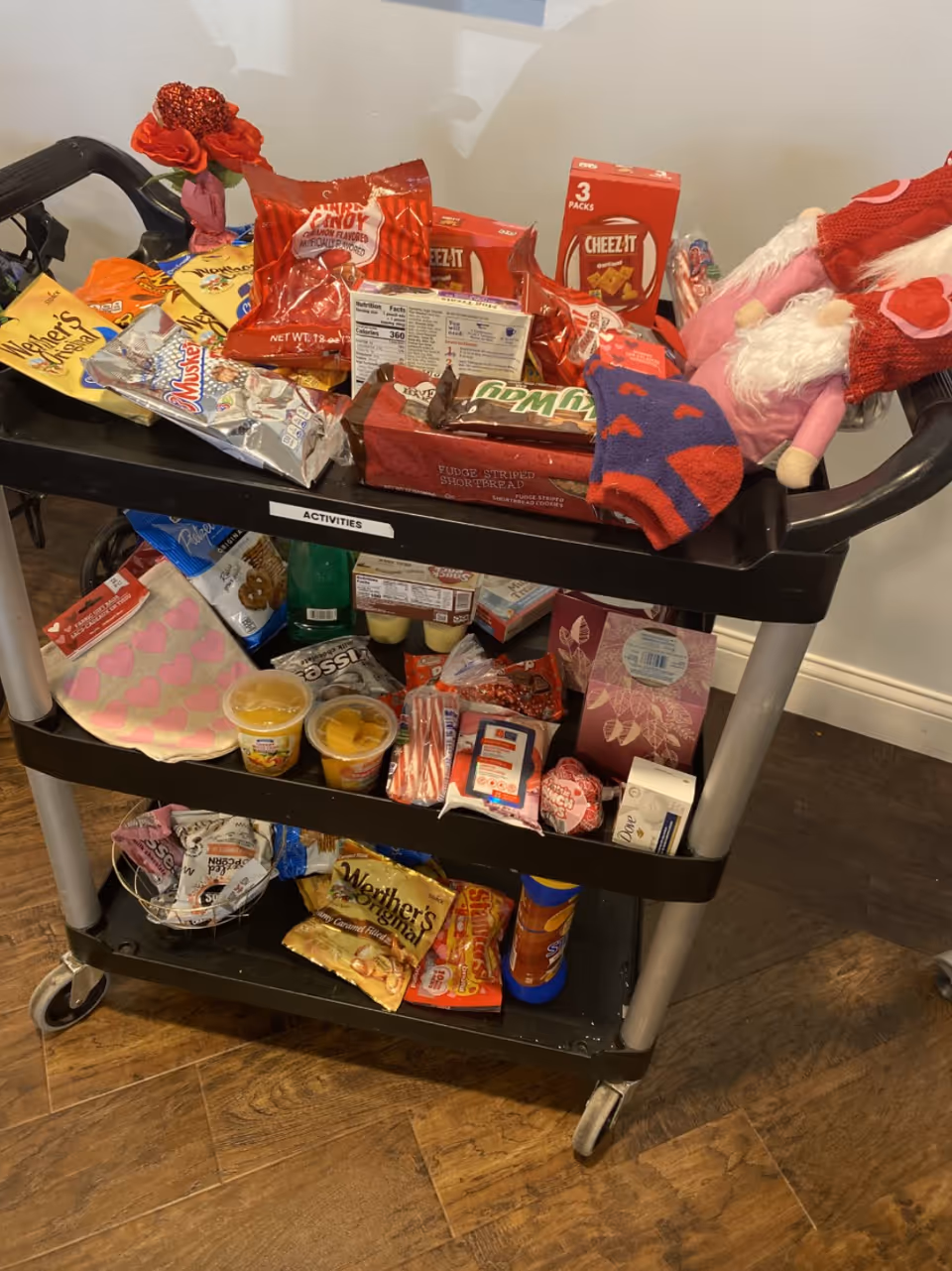 A multi-tier snack cart filled with assorted snacks and drinks in a senior living facility hallway.